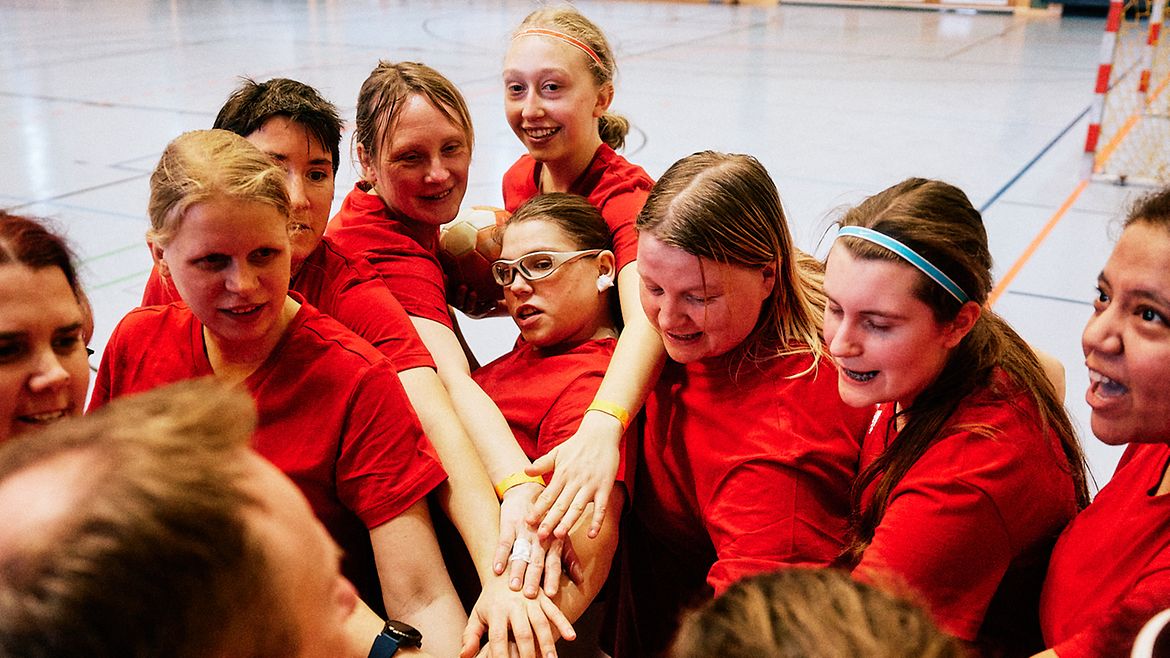 Die Handballerinnen stehen eng zusammen im Kreis und legen ihre Hände übereinander.