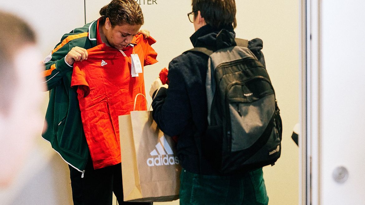 Sportlerin Crisdaian Abel hält ein T-Shirt vor ihren Körper. Neben ihr hält Gaby Grzonkowski eine Adidas-Tüte.