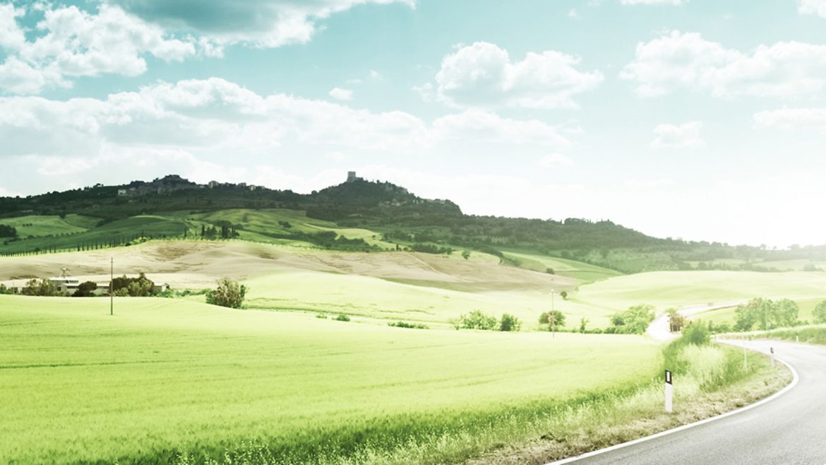 Landstraße durch eine hügelige Landschaft im Sommer.