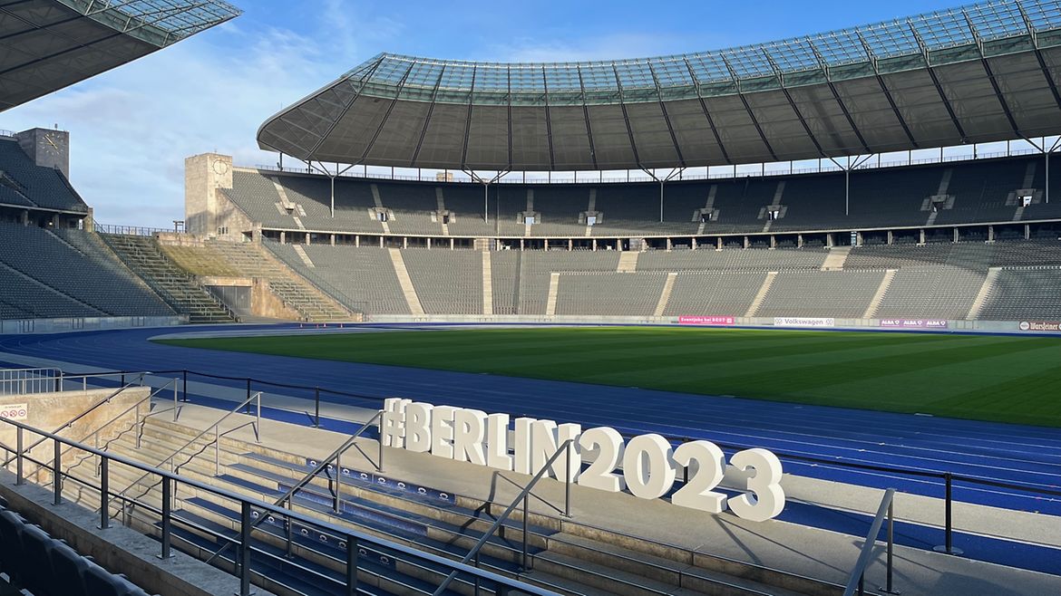 Blick ins Innere des Olympiastadions: Zuschauerränge, Rasenfläche, Laufbahnen, davor der Schriftzug #Berlin2023