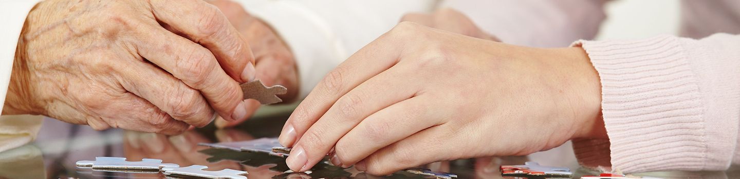 Hände von Seniorin und junger Frau mit Puzzle auf dem Tisch