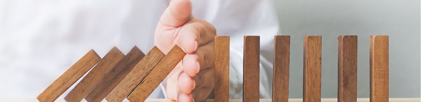 Hand hält eine Reihe umfallender Dominosteine auf.
