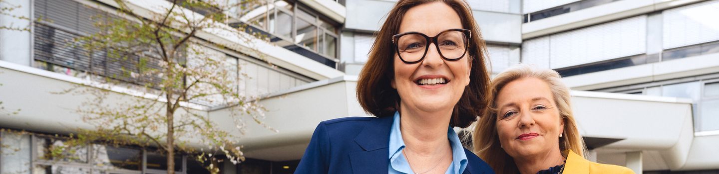 Zwei Frauen stehen lächelnd vor dem Gebäude der Hauptverwaltung der BGW in Hamburg.