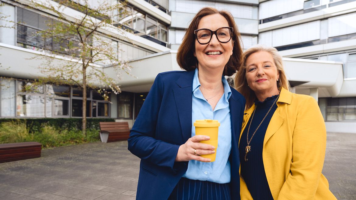 Zwei Frauen stehen lächelnd vor dem Gebäude der Hauptverwaltung der BGW in Hamburg.