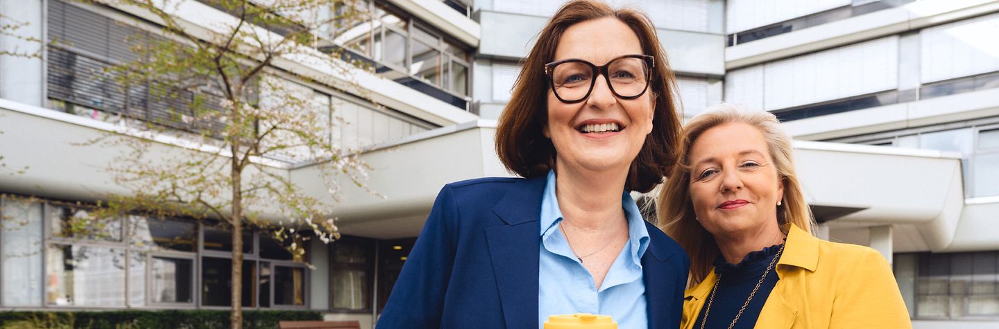Zwei Frauen stehen lächelnd vor dem Gebäude der Hauptverwaltung der BGW in Hamburg.