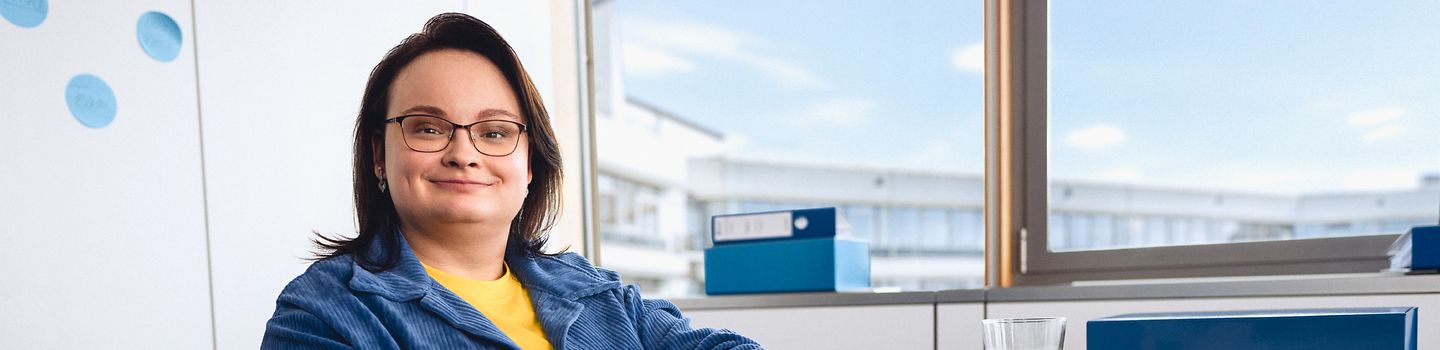 1000 UNDEIN GRUND - Für dein Können mehr als Respekt verdienen Eine Frau im Rollstuhl sitzt am Schreibtisch in einem Büro