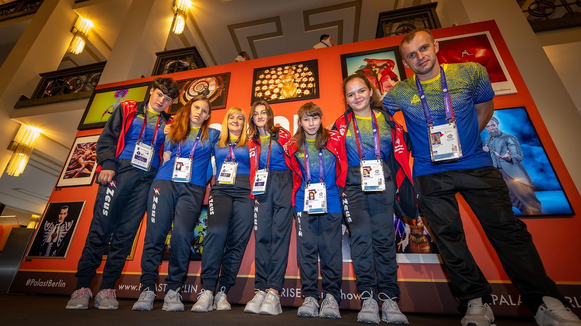 5 ukrainische Sportlerinnen und 2 Sportler im Friedrichstadtpalast vor einer Fotowand. Alle tragen gelb-blaue Trikots.