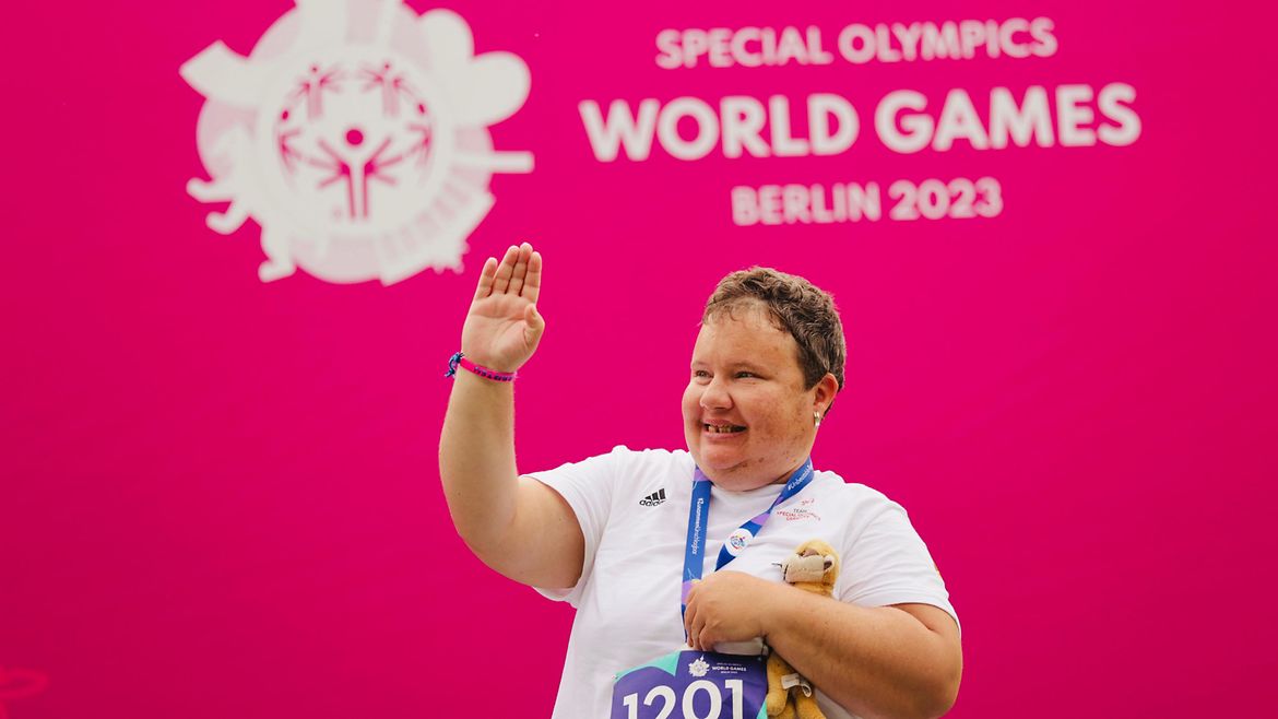 Miriam Klimetzek hat die Medaille um den Hals und hält sie mit einer Hand fest. Unterm Arm ein Kuscheltier, mit der anderen Hand grüßt sie.