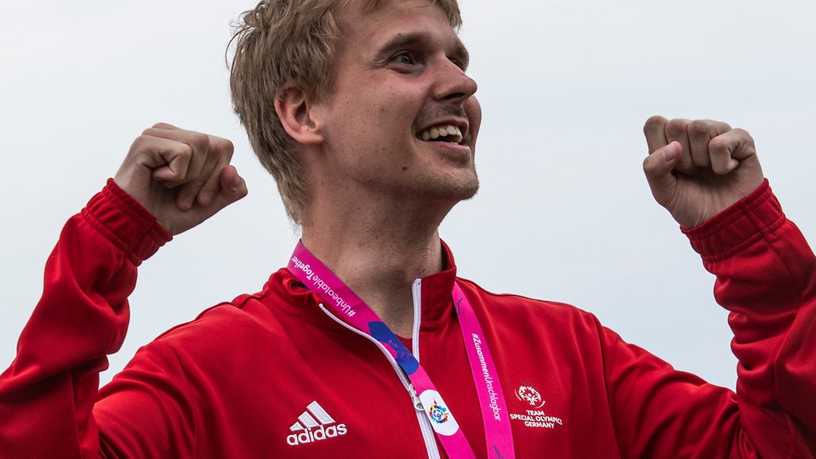 Kai-Jürgen Pönisch mit Goldmedaille in roter Trainingsjacke hebt in Siegerpose die Arme.