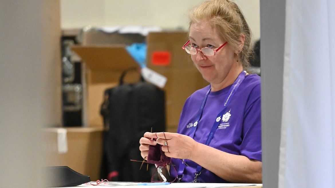 Birgit Müller sitzt an einem Tisch und hält Strickzeug in der Hand.