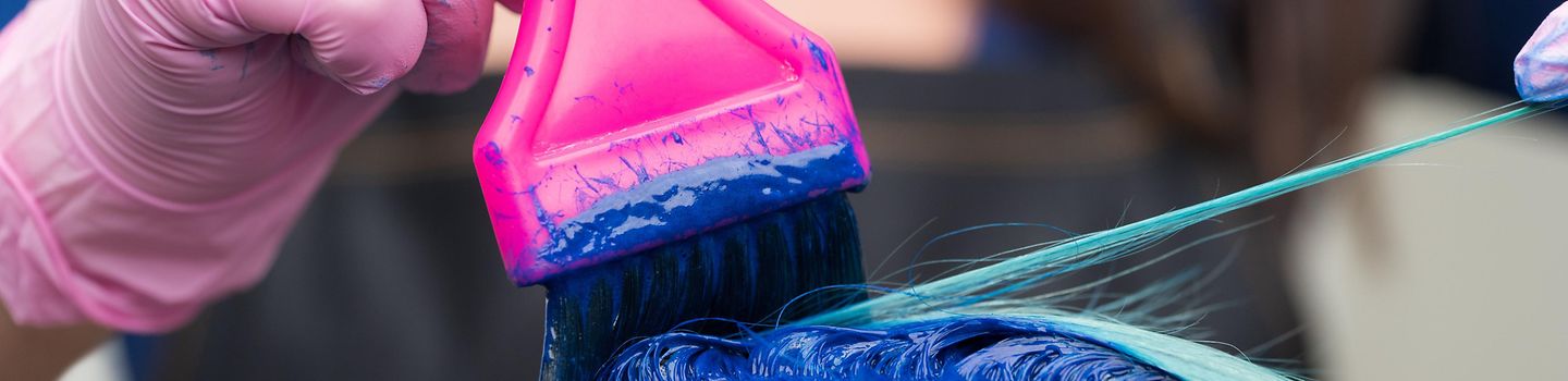 Haarefärben Friseurin trägt mit Schutzhandschuhen und Pinsel blau-grüne Haarfarbe auf das Haar einer Kundin auf