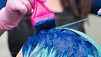 Friseurin trägt mit Schutzhandschuhen und Pinsel blau-grüne Haarfarbe auf das Haar einer Kundin auf
