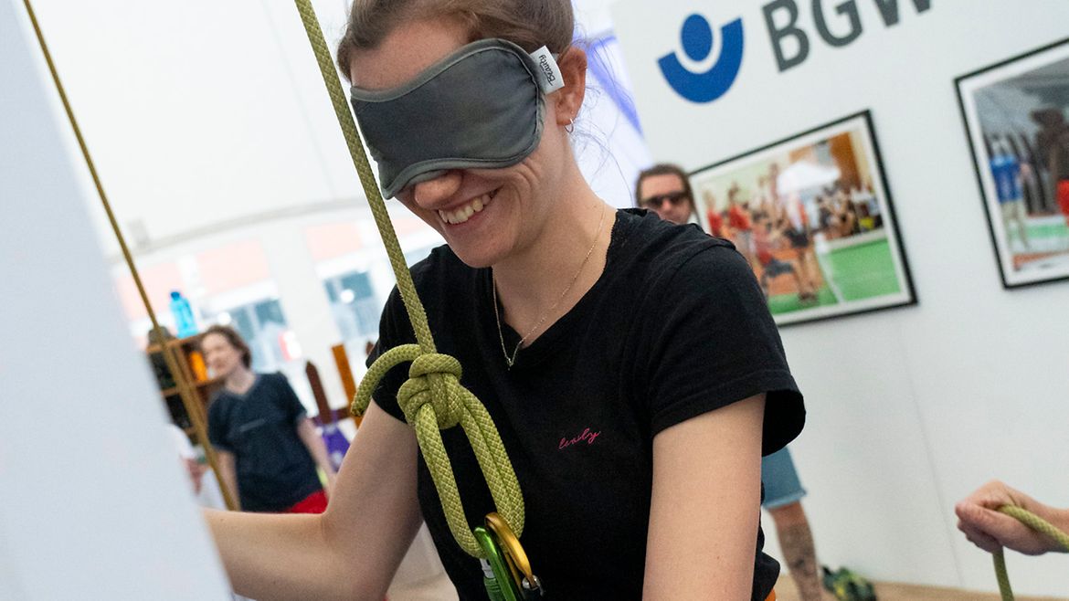 Eine angeseilte Besucherin inklusiven Kletterturm mit dunklem Sichtschutz auf den Augen