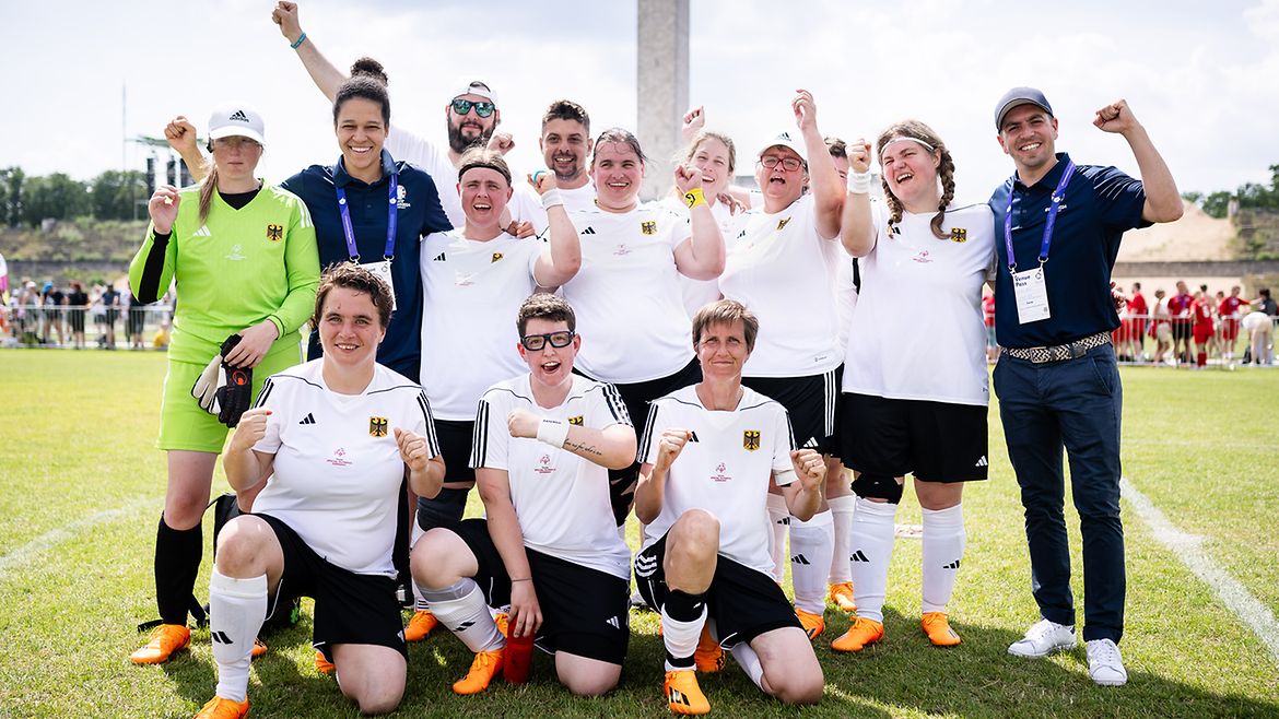 Die TeamSOD Frauen-Mannschaft steht in Trikots aufgereiht mit Philipp Lahm und Célia Šašić auf dem Rasen und streckt die Fäuste hoch