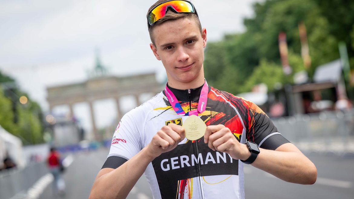 Leon Colberg hält mit beiden Händen seine Goldmedaille in die Kamera. Im Hintergrund das Brandenburger Tor.