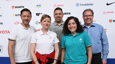 Zwei Frauen und drei Männer stehen vor einer Wand mit Sponsoren-Logos