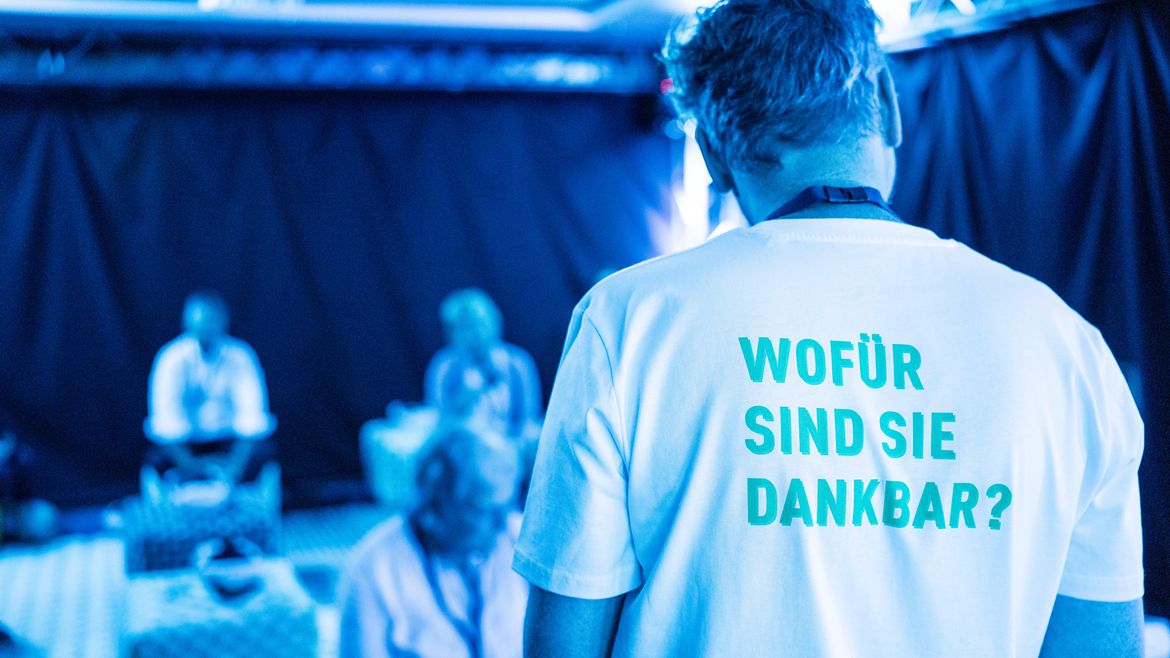 Rückenansicht eines Mannes, der ein T-Shirt mit der Aufschrift "Wofür sind Sie dankbar?" trägt.