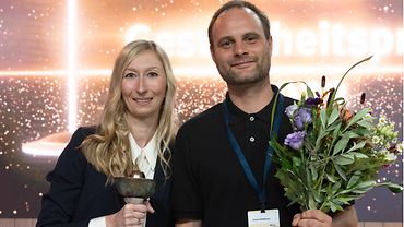Nicole Schröder und Simon Gaußmann halten den Siegerpokal und Blumen in den Händen.