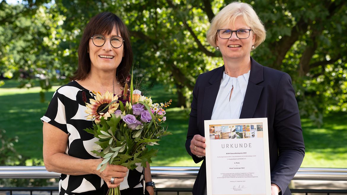 Heike Girard und Kirsten Gilling-Heggemann posieren mit Blumen und Urkunde in den Händen.