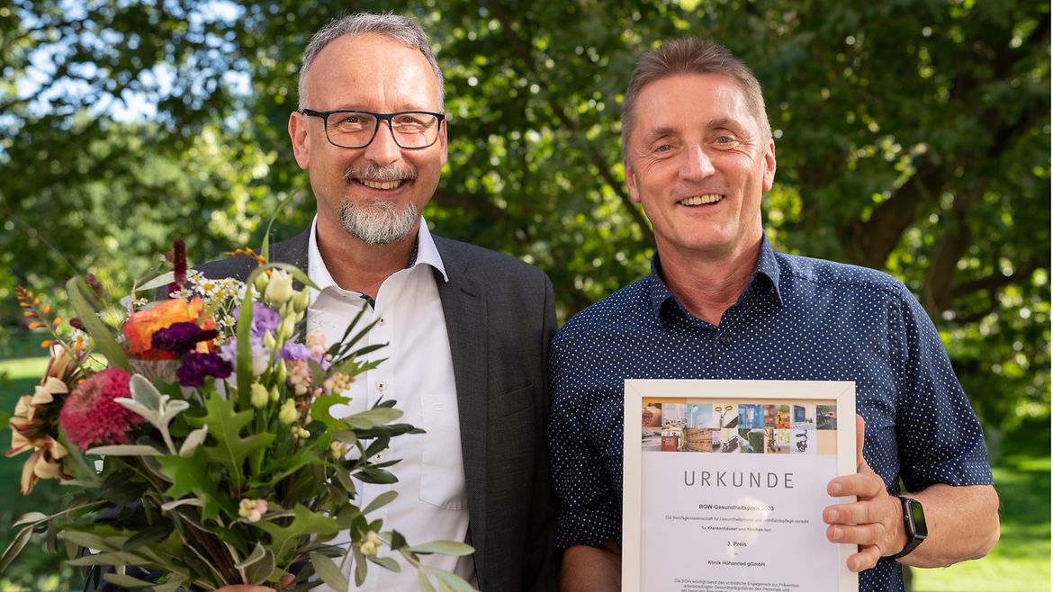 Robert Zucker und Jürgen Prochaska posieren mit Blumen und Urkunde in den Händen.