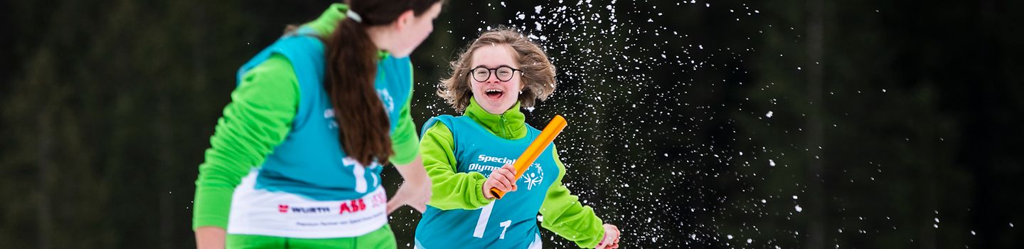 Special Olympics Nationale Spiele Thüringen 2024 Zwei Frauen mit Schneeschuhen übergeben sich ein Staffelholz im Schnee.