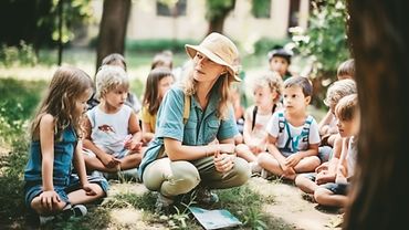 Eine Gruppe Kinder und eine junge Frau sitzen auf einer Wiese.