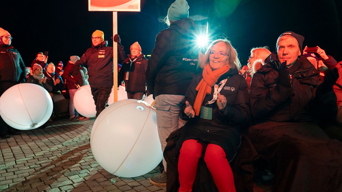 Im Vordergrund sitzen die SOD-Präsidentin und der Sportminister. Links daneben laufen zwei Athleten mit einem Schild "Thüringen" durch die Menge. Helfende am Rand halten große, weiße Bälle.